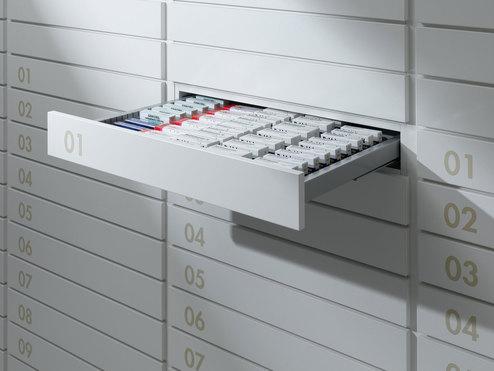 Detailaufnahme von schmalen weißen Medikamentenschubläden mit dezenter Nummerierung und sichtbarer Medikamentenaufteilungen.