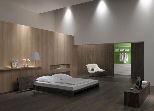 Schlafzimmerimpression von Bett, Nachtisch und Sideboard mit Holzverkleidung an Wand und indirektert Beleuchtung